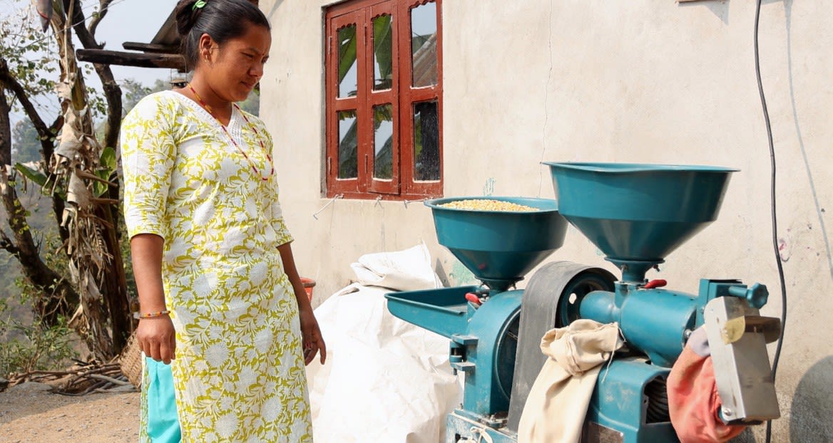 A Chepang woman stands next to a grinding mill.